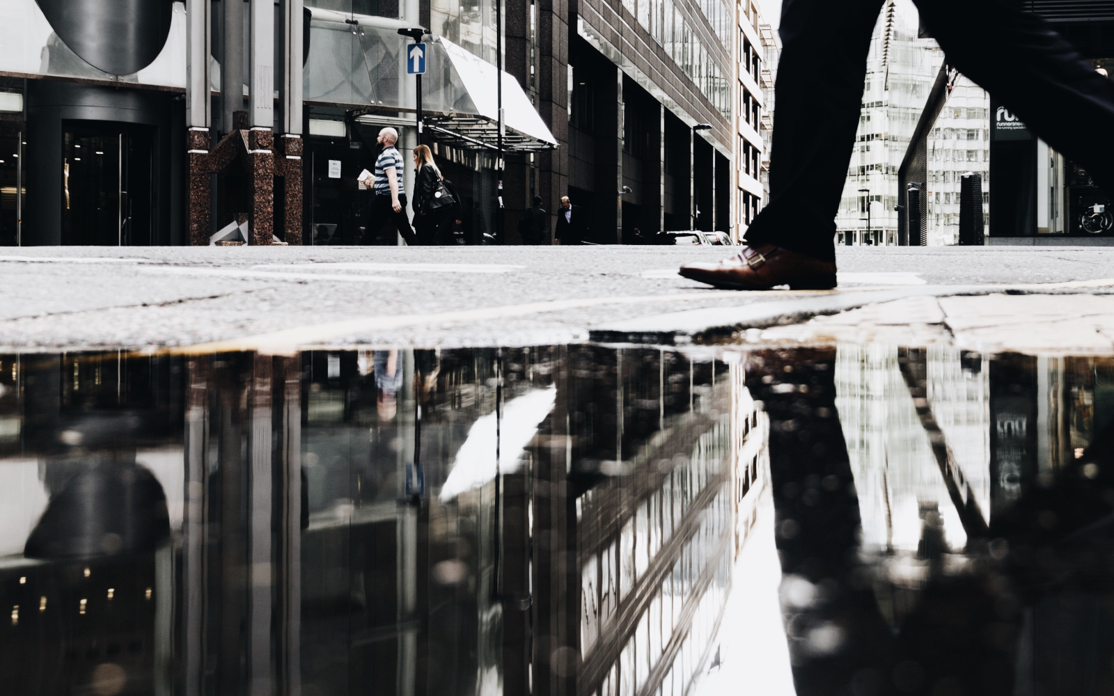 A man walking with his reflection in a water pond in the street